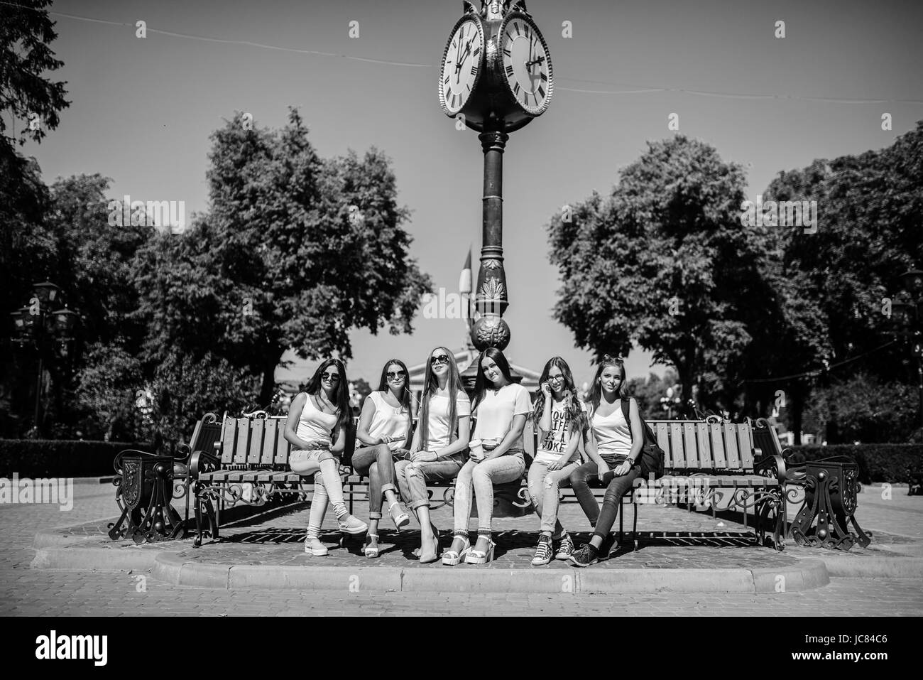 Six beautiful young girls sitting on a bench next to the old street clock in the park. Black and white photo. Stock Photo
