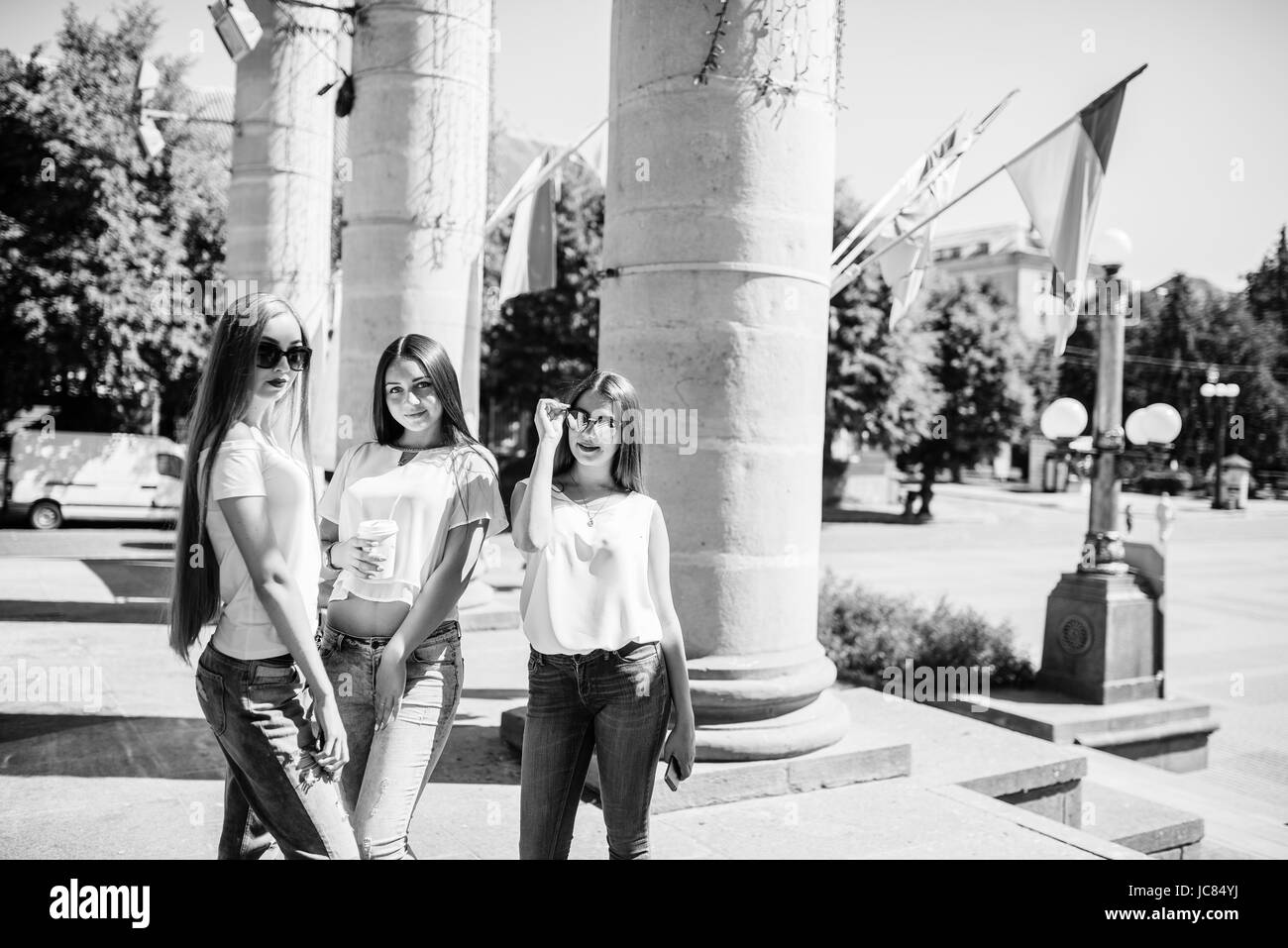 Three gorgeous girls standing by the columns on a sunny day. Black and white photo. Stock Photo