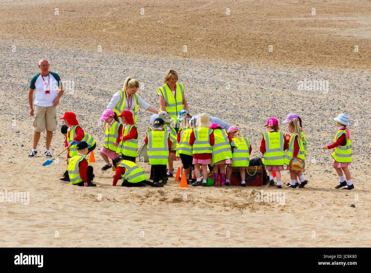 In Blackpool, Fylde Coast, Lancashire, UK, school children, wearing safeguarding hi-visibility vests are escorted on a primary school field trip in June weather in the United Kingdom. With morning temperatures already in the 20's, these youngsters are well protected against the sun's rays as they begin on a treasure hunt on the shore in reflective apparel. Stock Photo