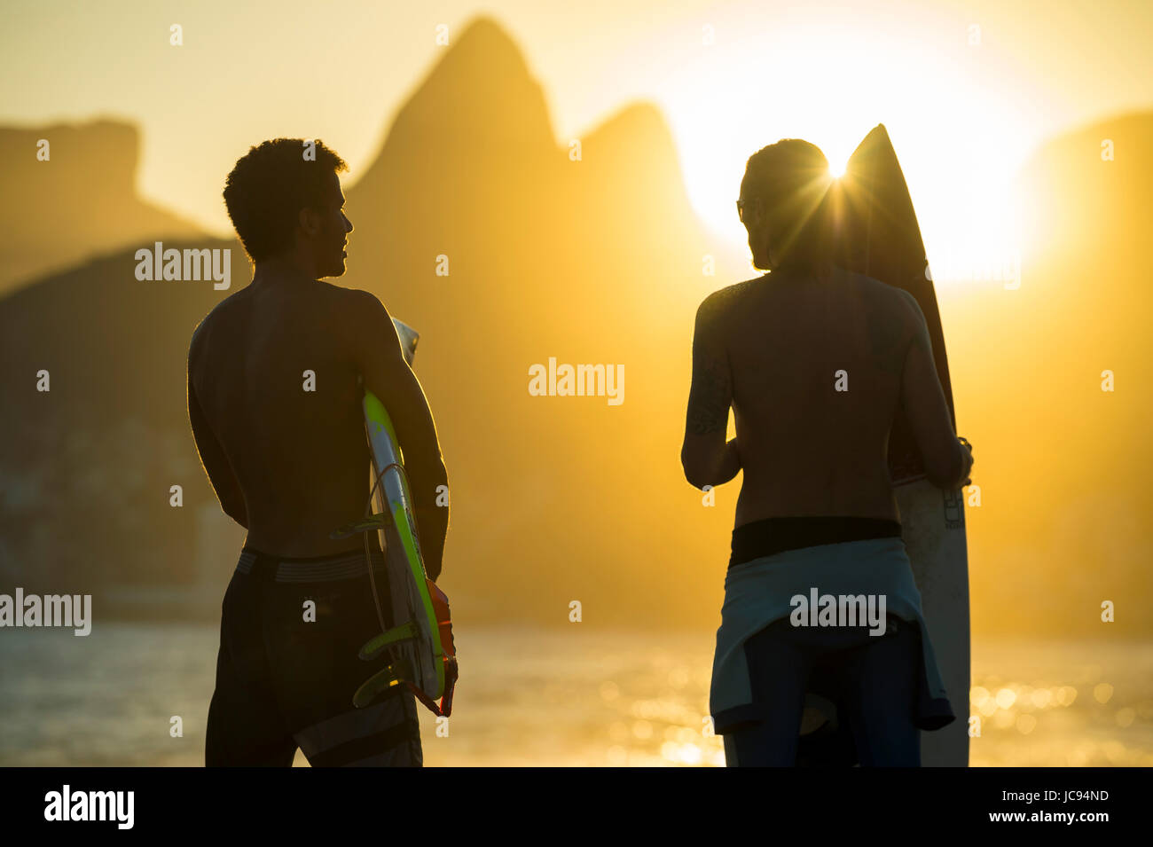 RIO DE JANEIRO - MARCH 20, 2017: Sunset silhouettes of two young surfers with surfboards at Arpoador with two brothers mountains in the background Stock Photo
