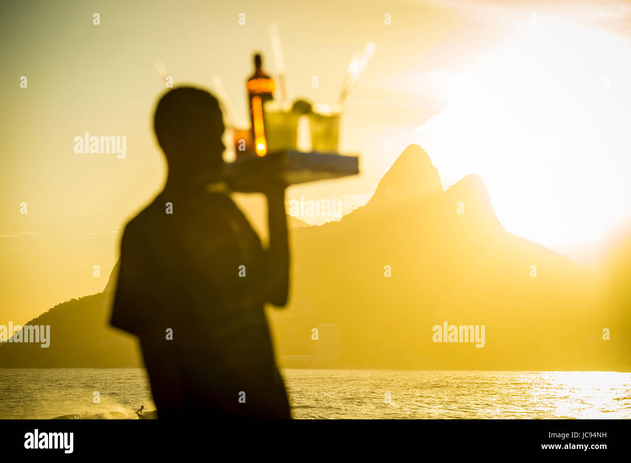 Defocused silhouette of a caipirinha vendor working at Arpoador during a golden sunset with focus on Two Brothers Mountain in the background. Stock Photo