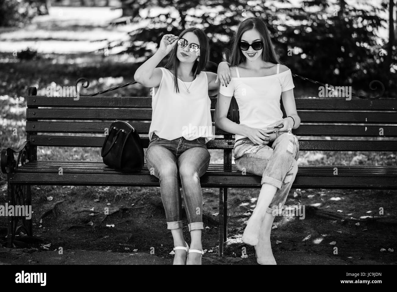 Two fabulous girls sitting on the bench in the park. Black and white photo. Stock Photo