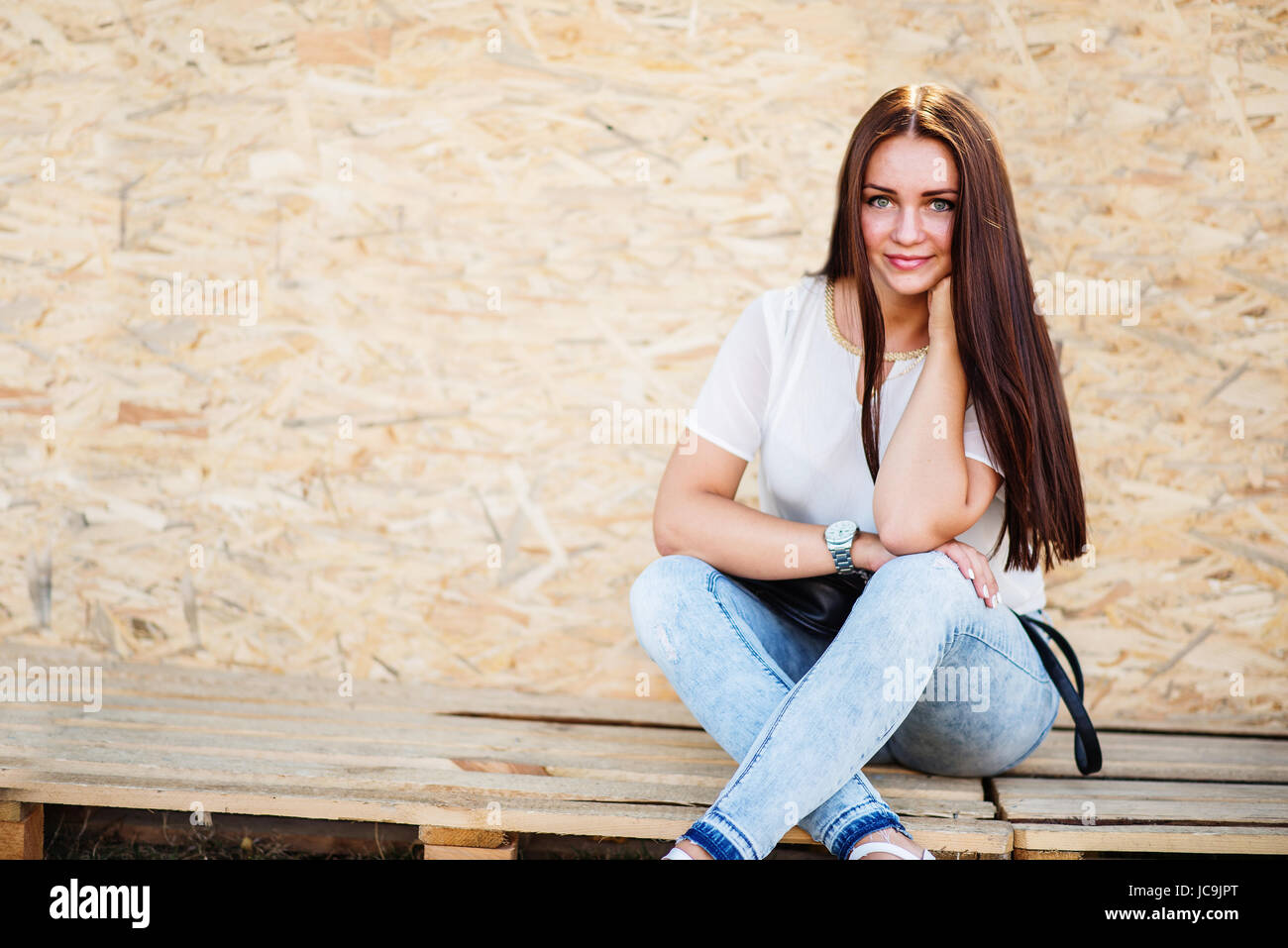 Portrait of a beautiful girl sitting on wooden boards against veneer ...