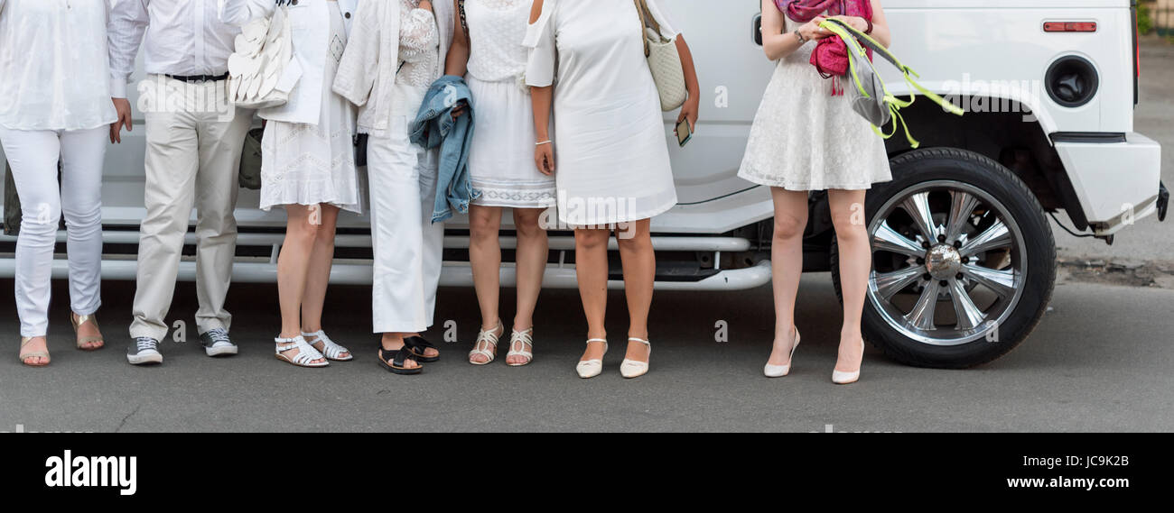 People dressed in white posing next to limousine. Body parts, white party Stock Photo