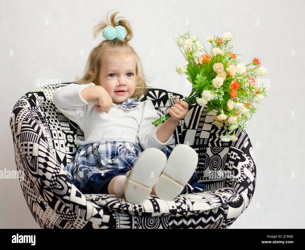 A little girl sitting on a chair with a bouquet of artificial flowers ...