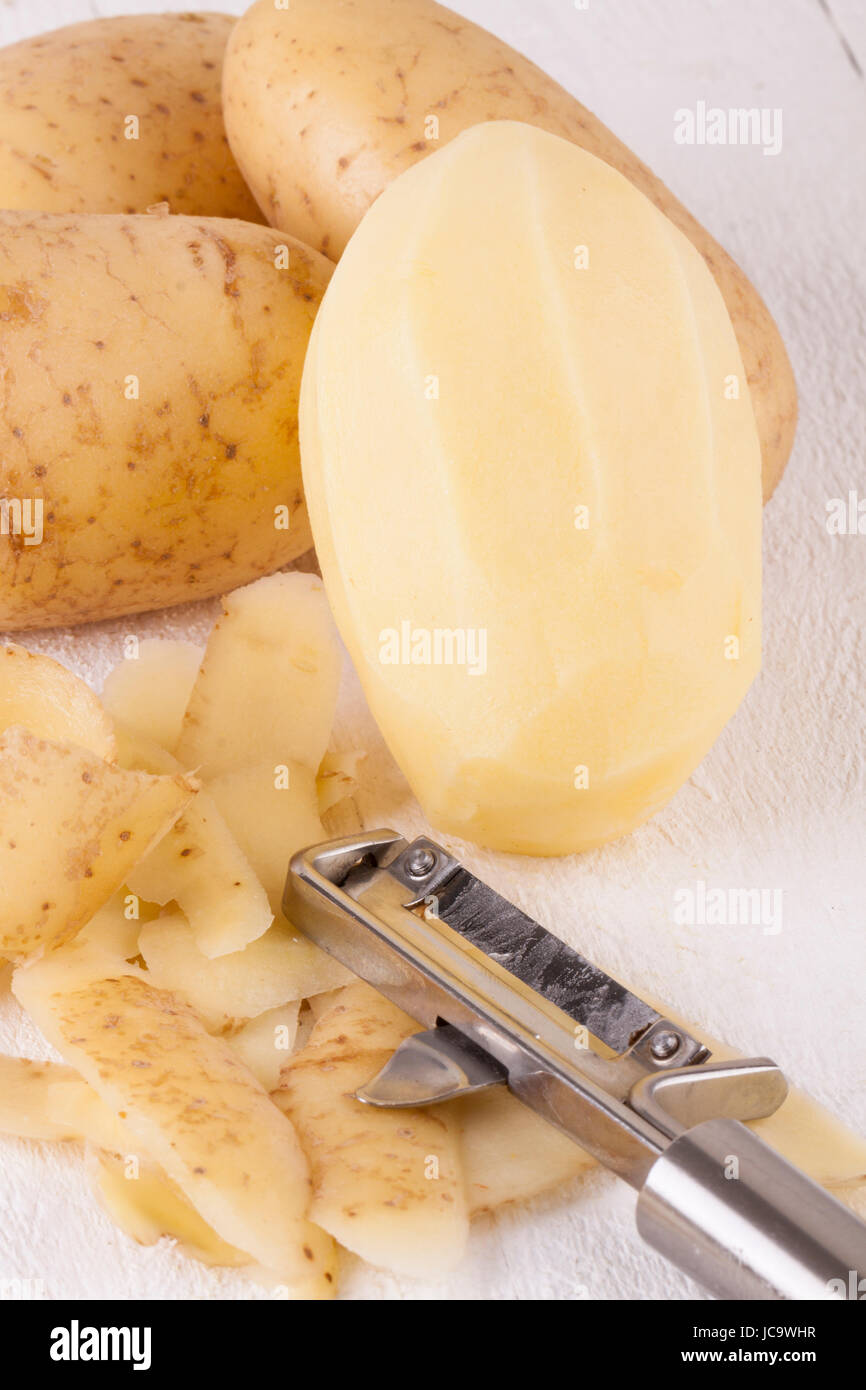 Kartoffeln mit Schalen und geschält mit Kartoffelschäler Sparschäler als Nahaufnahme Stock Photo