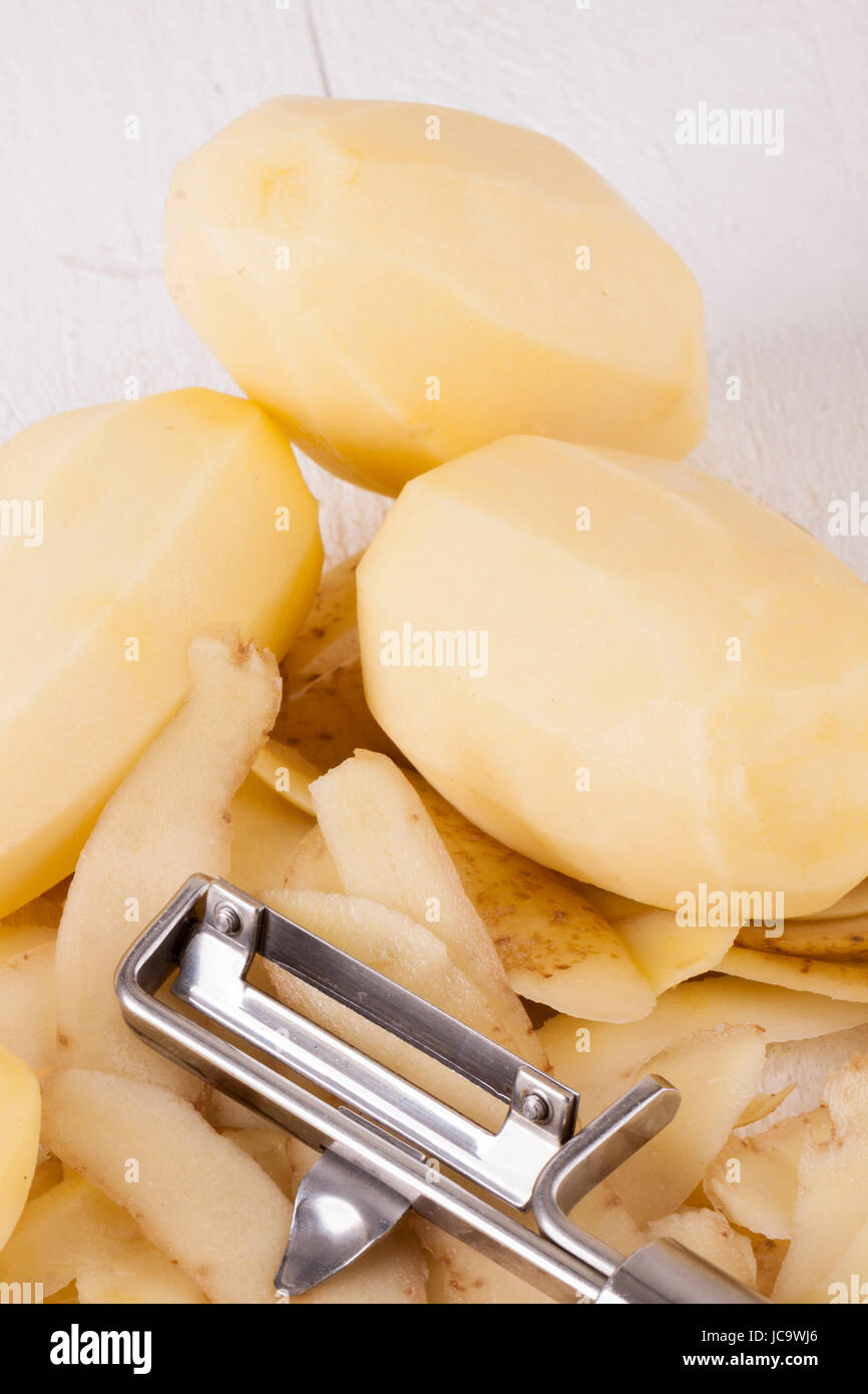 Kartoffeln mit Schalen und geschält mit Kartoffelschäler Sparschäler als Nahaufnahme Stock Photo