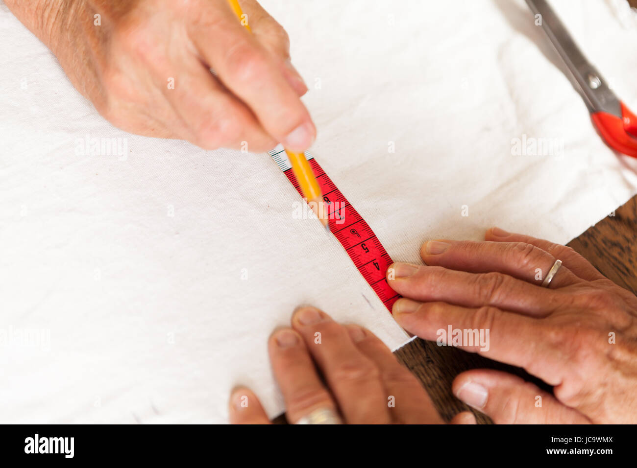 Hände mit Messband schere und Stift beim abmessen von Stoff für die Schneiderei Textil als Nahaufnahme Stock Photo