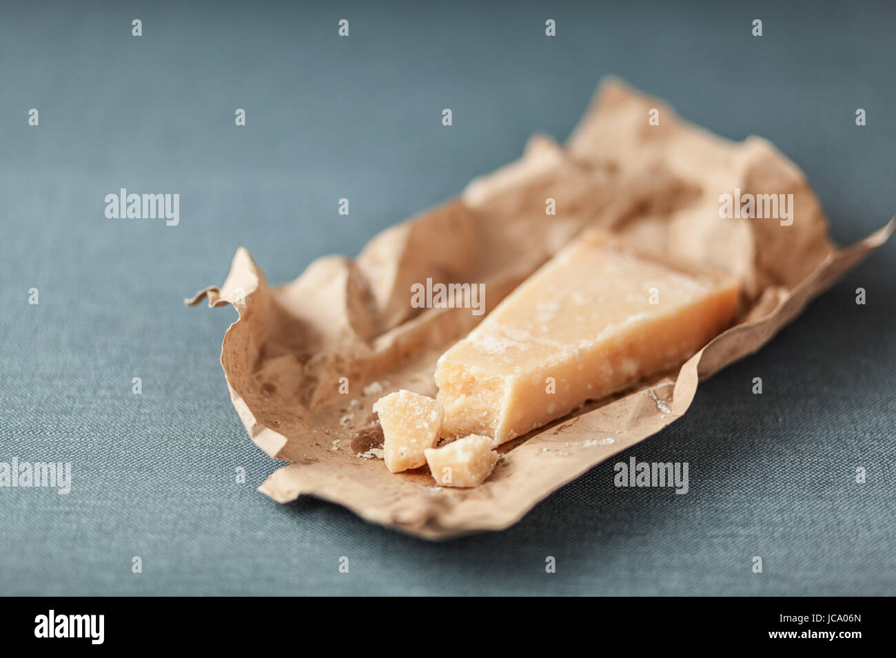 Wedge of hard Italian Parmigian-reggiano cheese on a torn brown paper wrapper for use as a cooking ingredient on a grey textile with copyspace Stock Photo