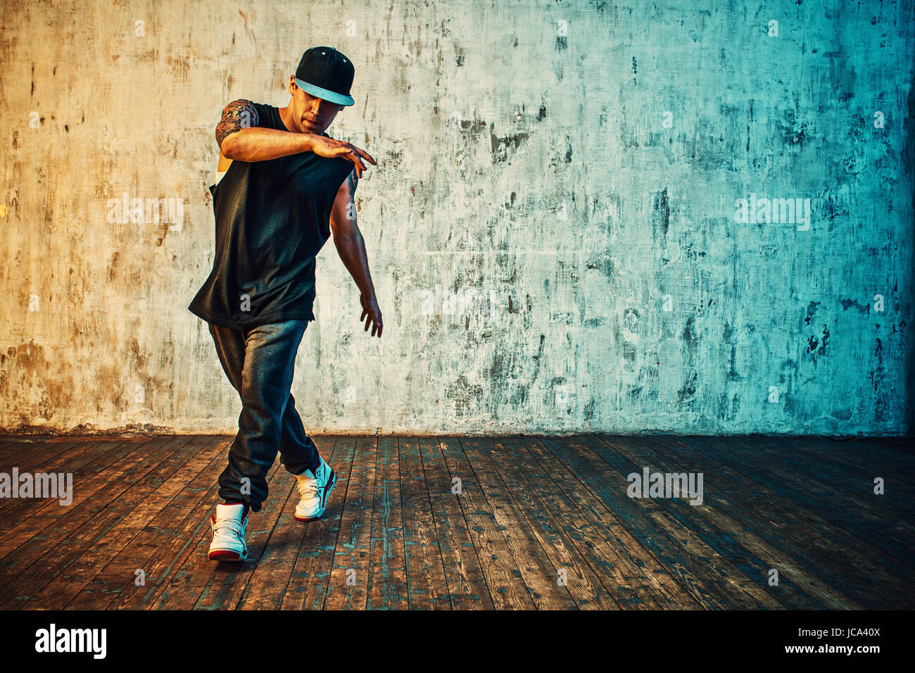 Young man break dancing on wall background. Vibrant colors effect. Tattoo on body. Stock Photo