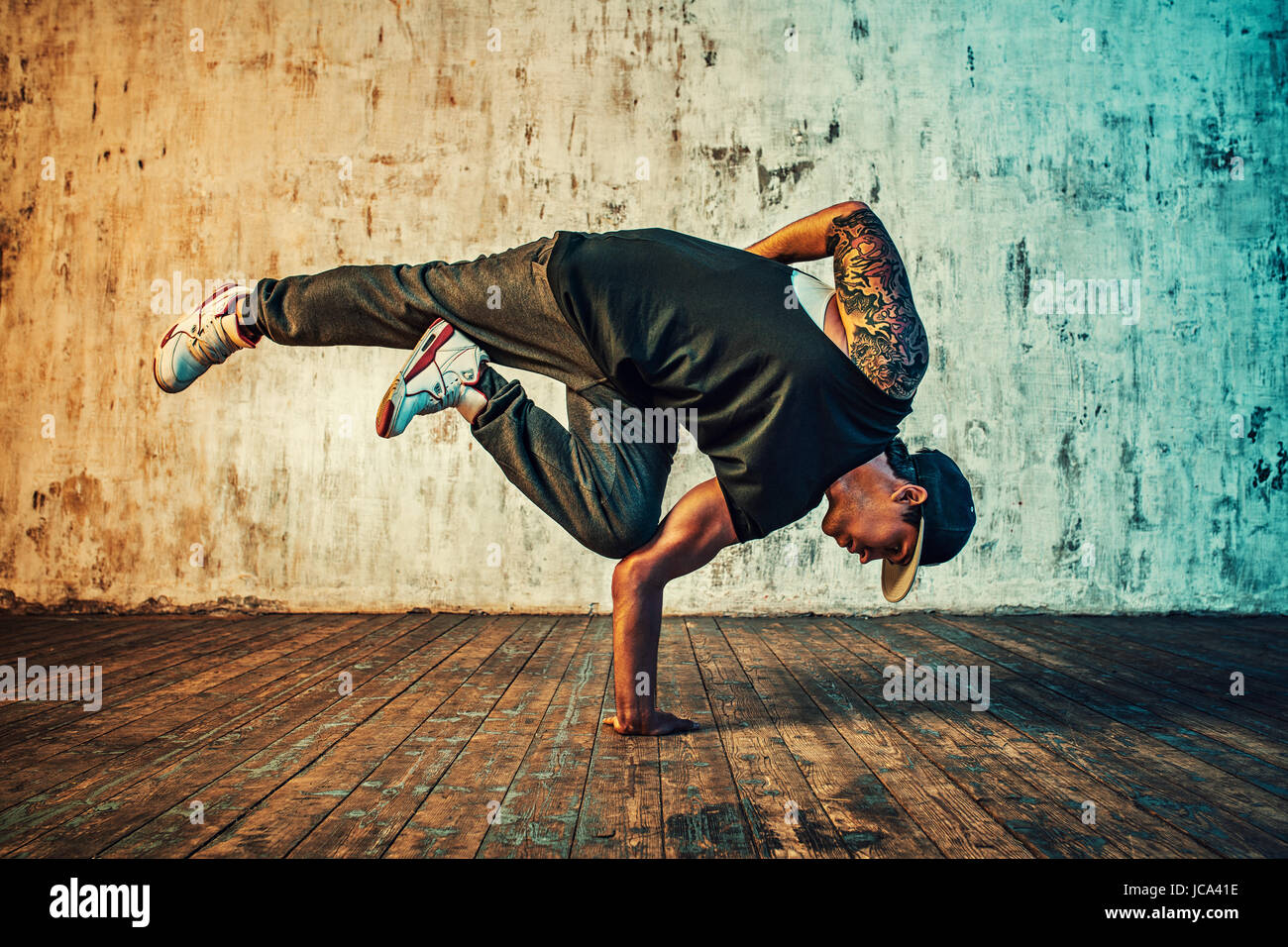 Young man break dancing on wall background. Vibrant colors effect. Tattoo on body. Stock Photo