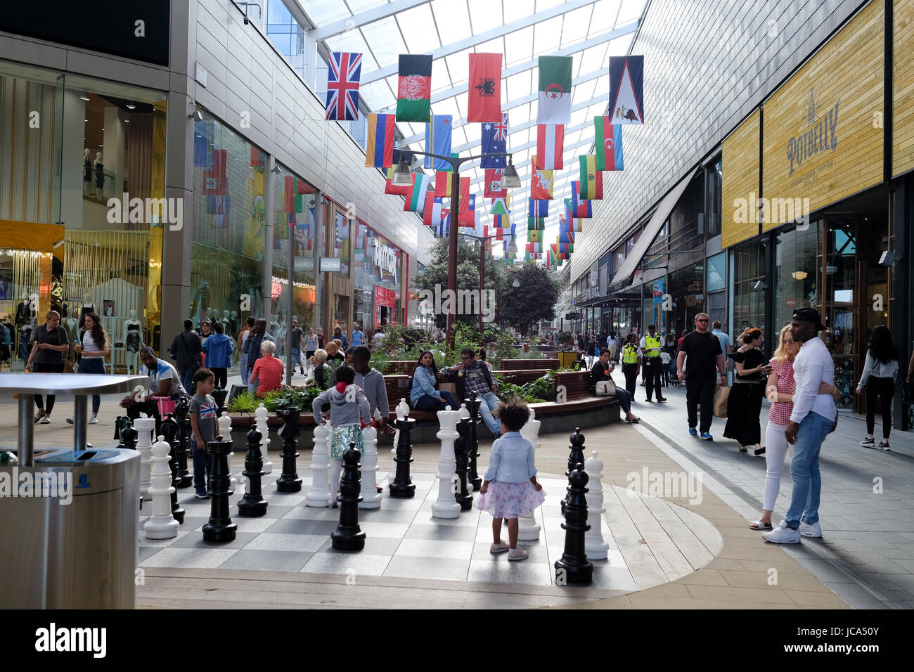 Children are playing at the chess playground in Westfield Stratford City shopping centre; World flags are hanging above along the corridor Stock Photo