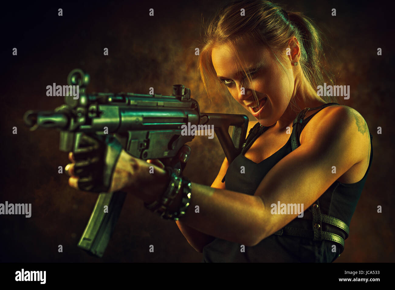 Young strong woman with big gun in dramatic urban interior. Tattoo on body  Stock Photo - Alamy