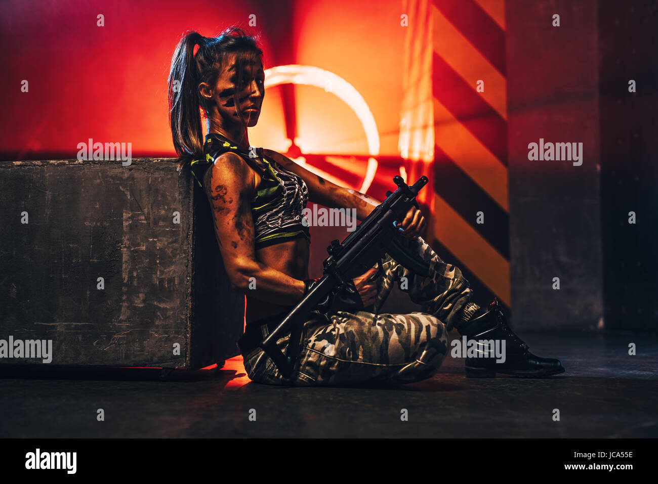 Young strong woman warrior with big gun in dramatic urban interior with red light Stock Photo