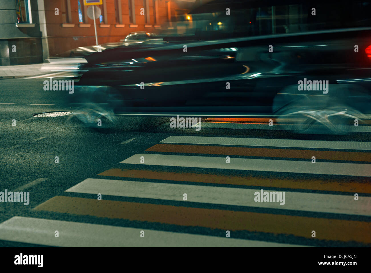 Crosswalk in city with fast moving blurred car at night. Pedestrian safety concept. Stock Photo