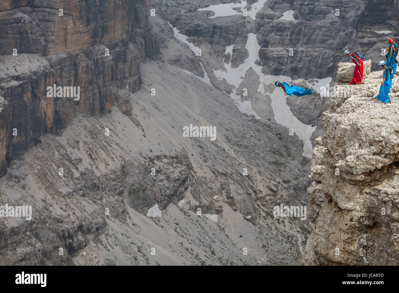 A group of base jumpers stand ready as one pilot takes flight in the Sass Pordoi region of the Dolomites. Italy. Stock Photo
