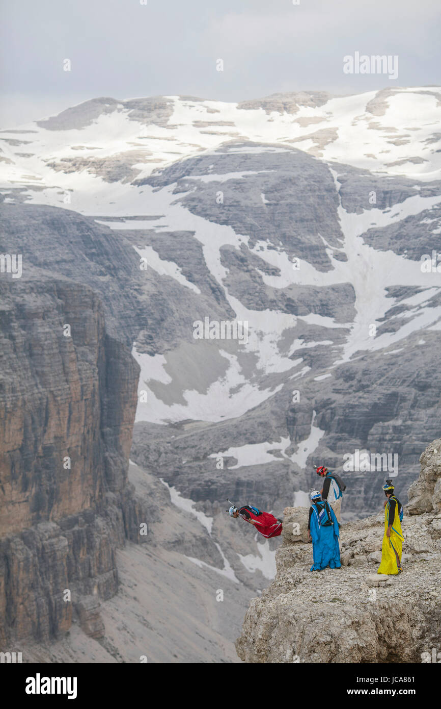 A group of BASE jumpers stand ready as one pilot takes flight in the Sass Pordoi region of the Dolomites. Italy. Stock Photo