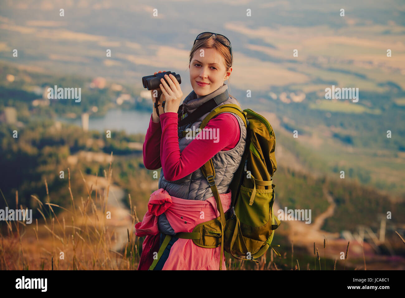 Young woman tourist standing with binoculars on mountain portrait Stock Photo