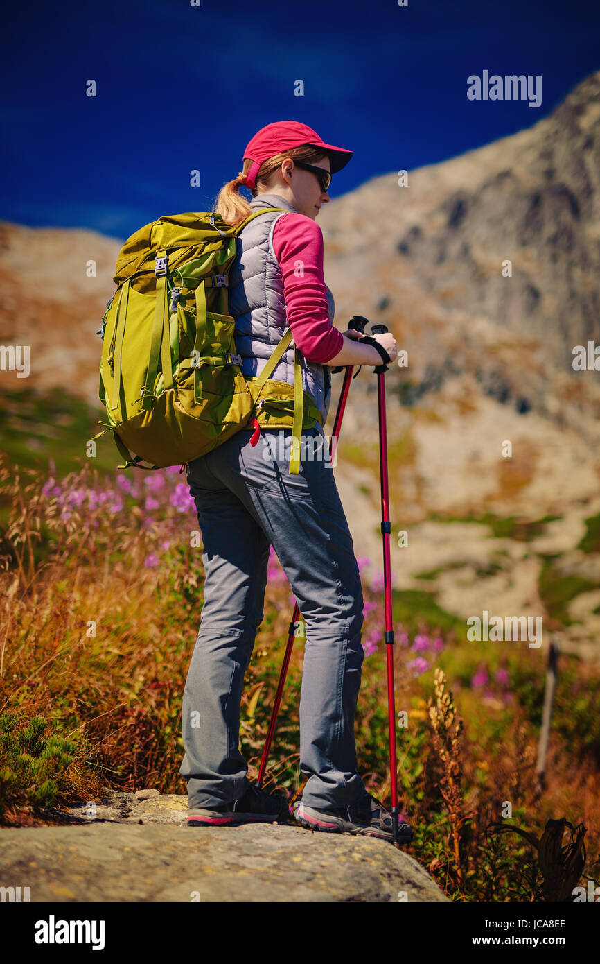 Young woman tourist with green backpack and sunglasses standing on high mountains background Stock Photo