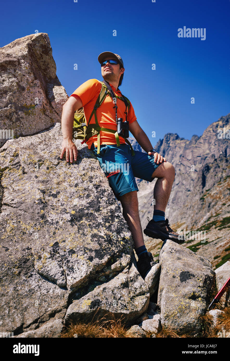 Young man tourist standing at high mountains and looking aside Stock Photo