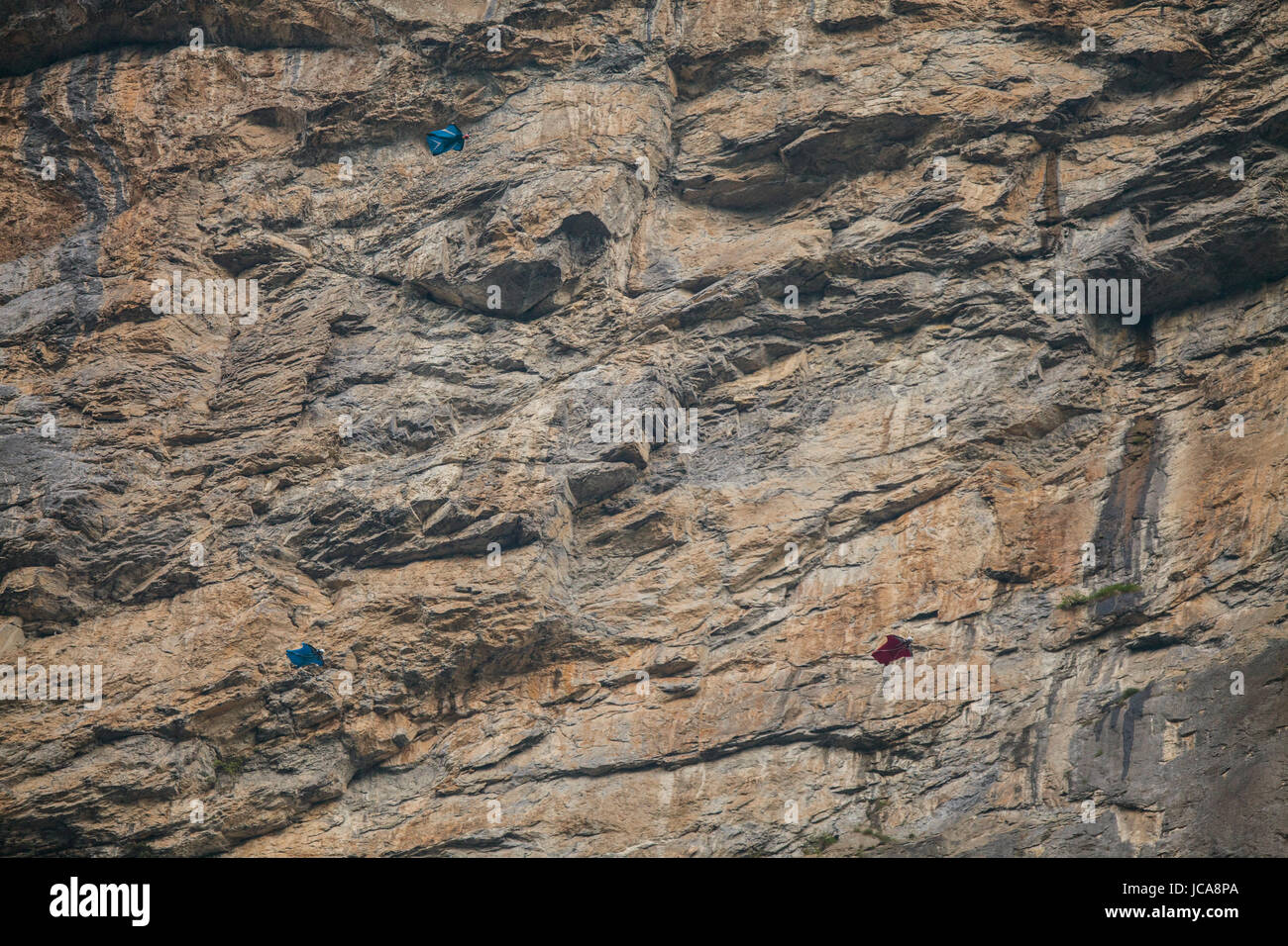 Three base jumpers in flight with a huge rock wall backdrop.  Toggenburg, Switzerland. Stock Photo