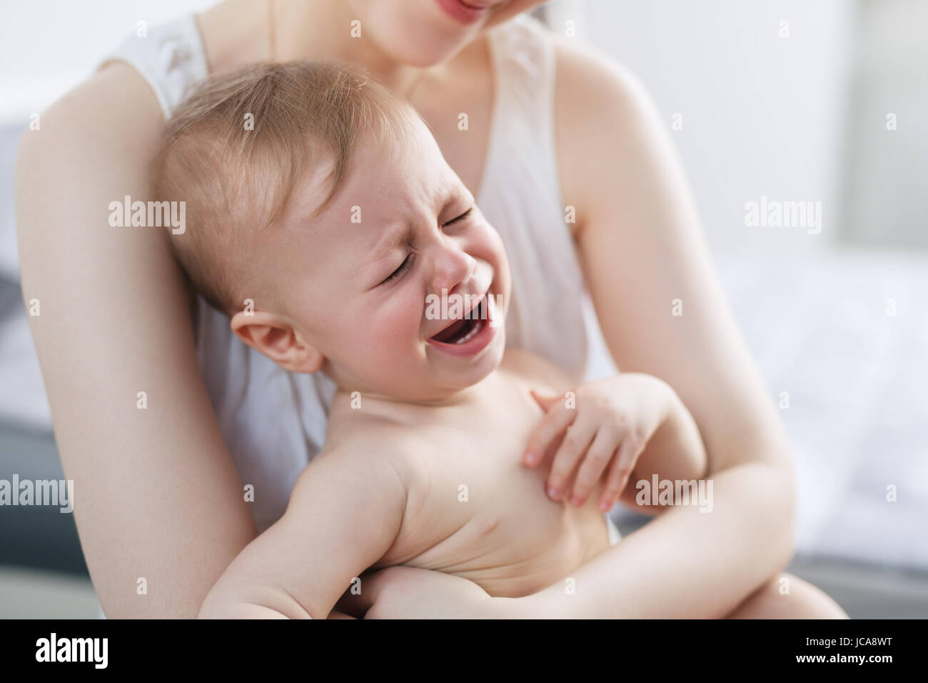 Young woman with crying baby on hands. Bright white colors. Stock Photo