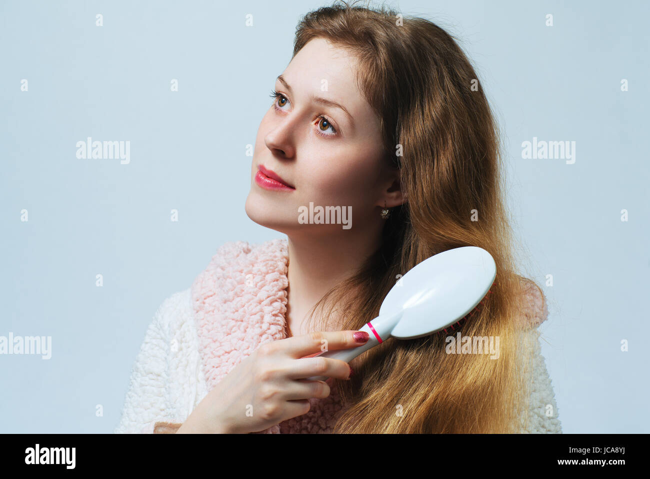 Young blond woman in bathrobe comb hair after washing. On white background. Stock Photo