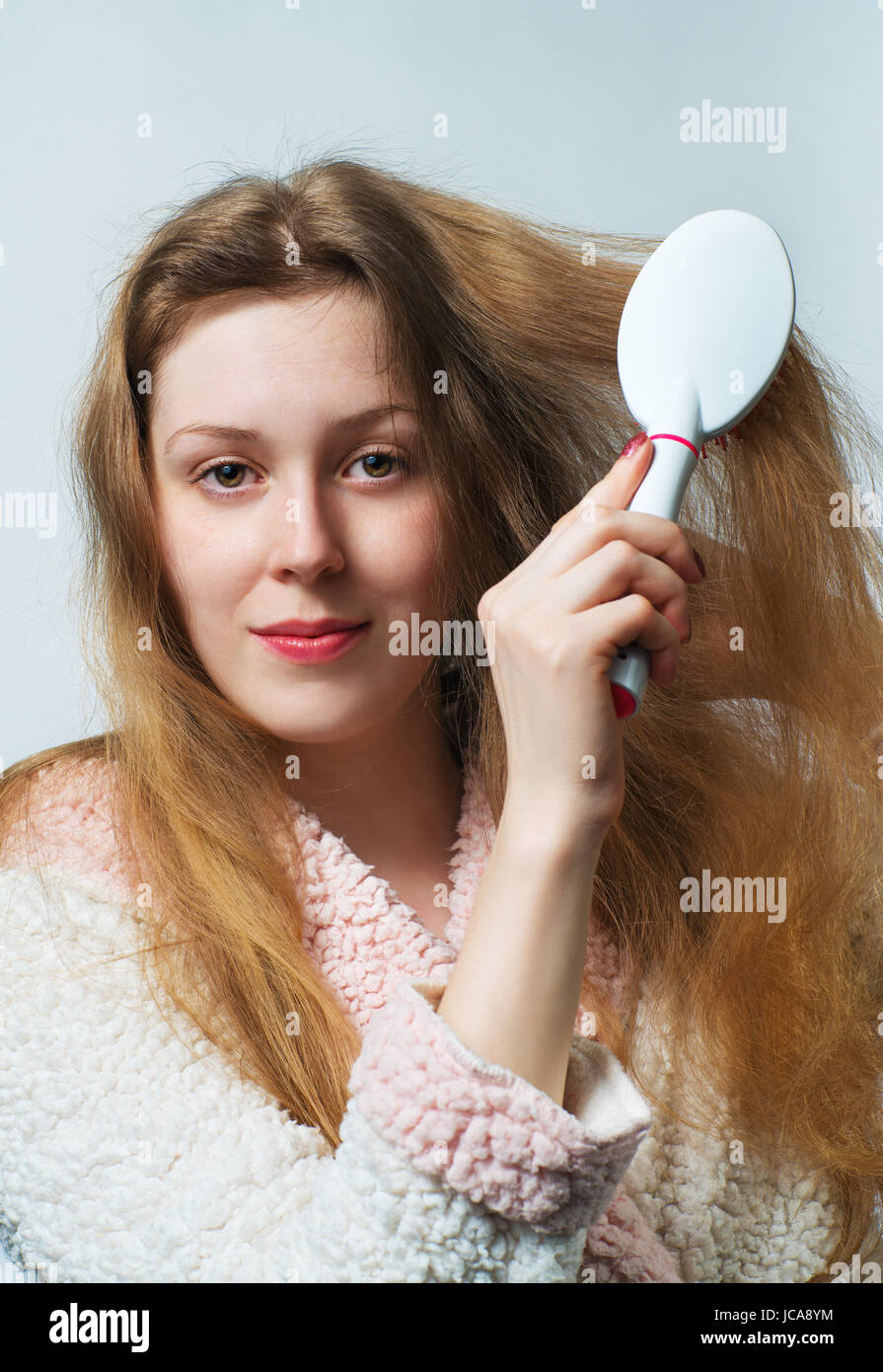 Young blond woman in bathrobe comb hair after washing. On white background. Stock Photo