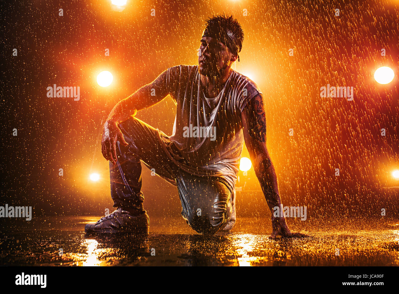 Young man break dancing in club with lights, water and smoke. Tattoo on body. Stock Photo