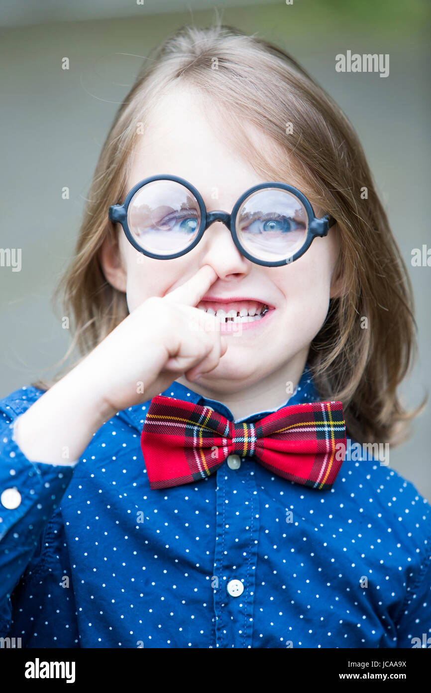 funny portrait of boy with bow tie and big glasses picking his nose