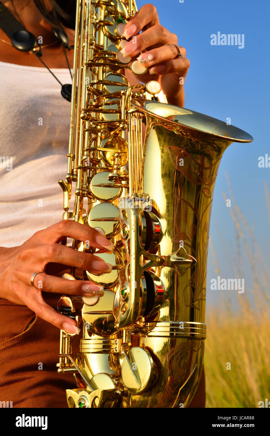 Women's hands hold a saxophone and play on it against the backdrop of nature Stock Photo