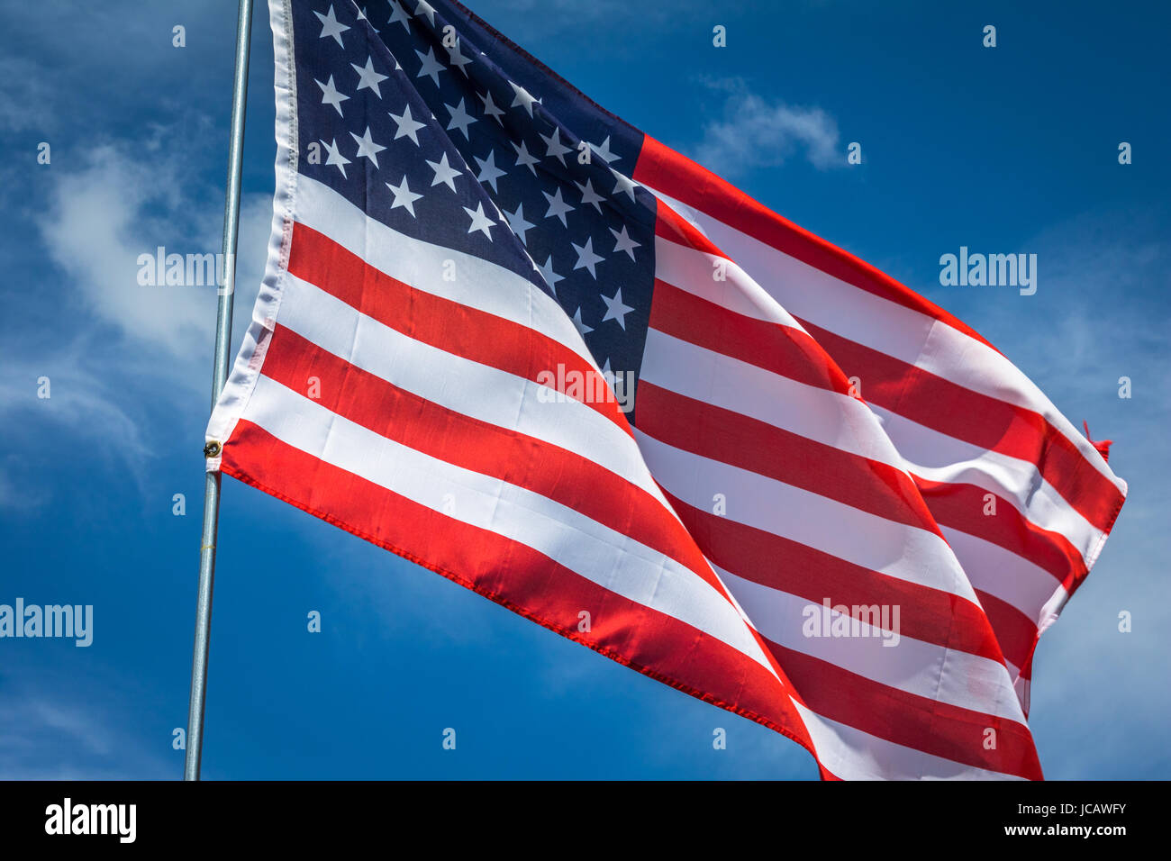 Horizontal photo of a red, white and blue American flag on a silver pole waving in the breeze Stock Photo