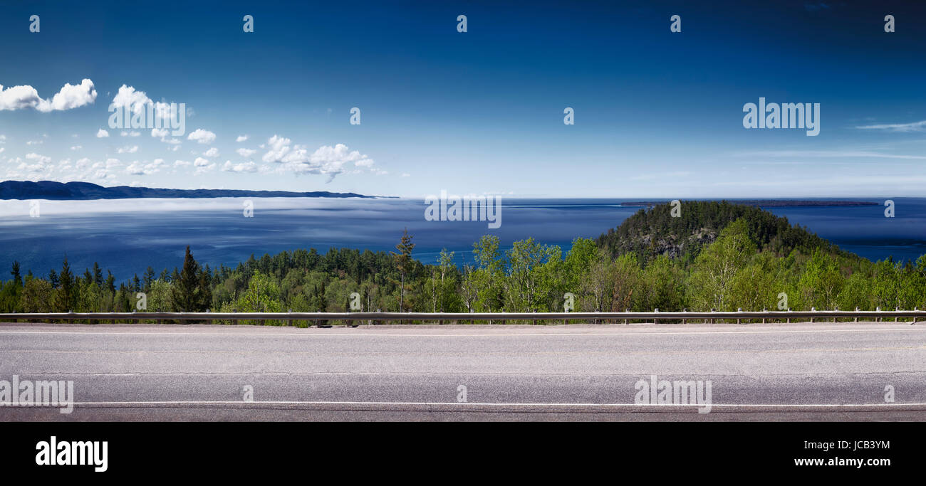 Panorama of Trans-Canada highway with blue sky over misty Lake Superior nature scenery in the background. Ontario, Canada. Stock Photo