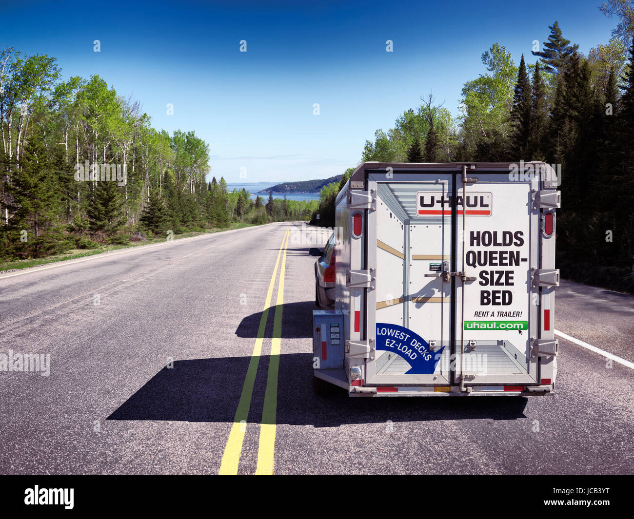 License available at MaximImages.com - Rear view of a car with a rental U-Haul UHAUL cargo trailer driving on a highway, transportation and moving Stock Photo