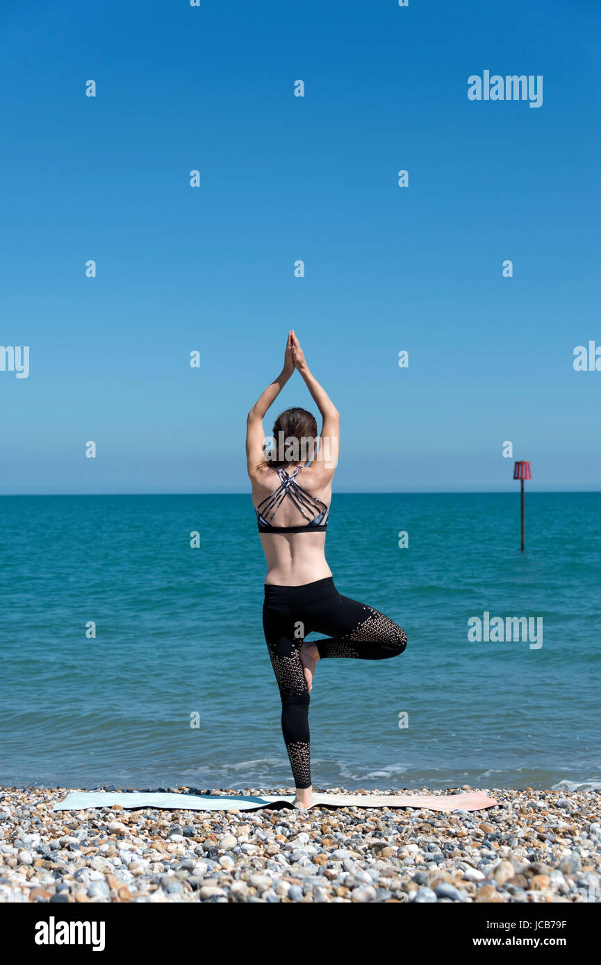 woman standing by the sea doing yoga, standing tree pose. Stock Photo