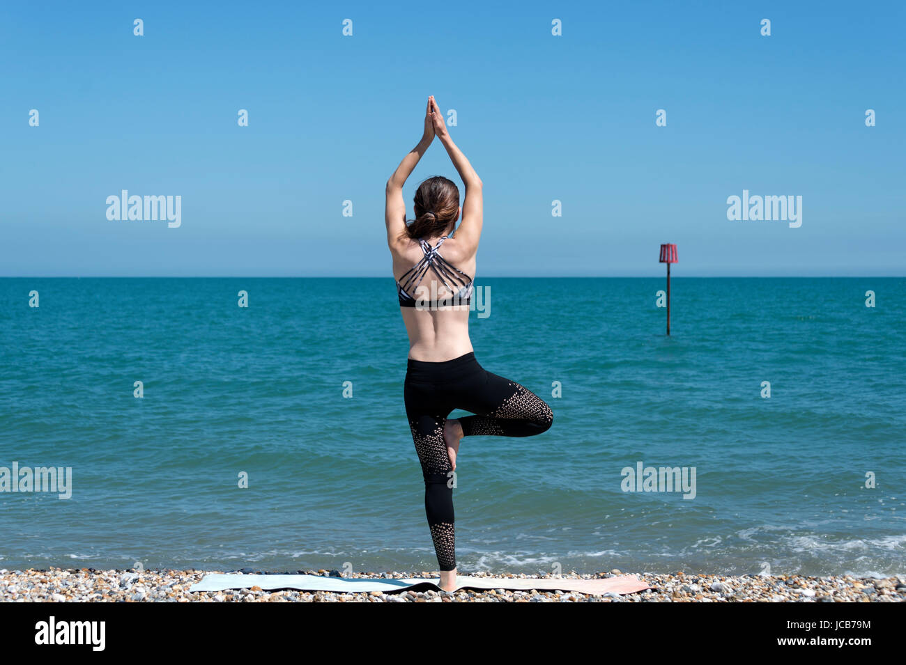 woman standing by the sea doing yoga, standing tree pose. Stock Photo