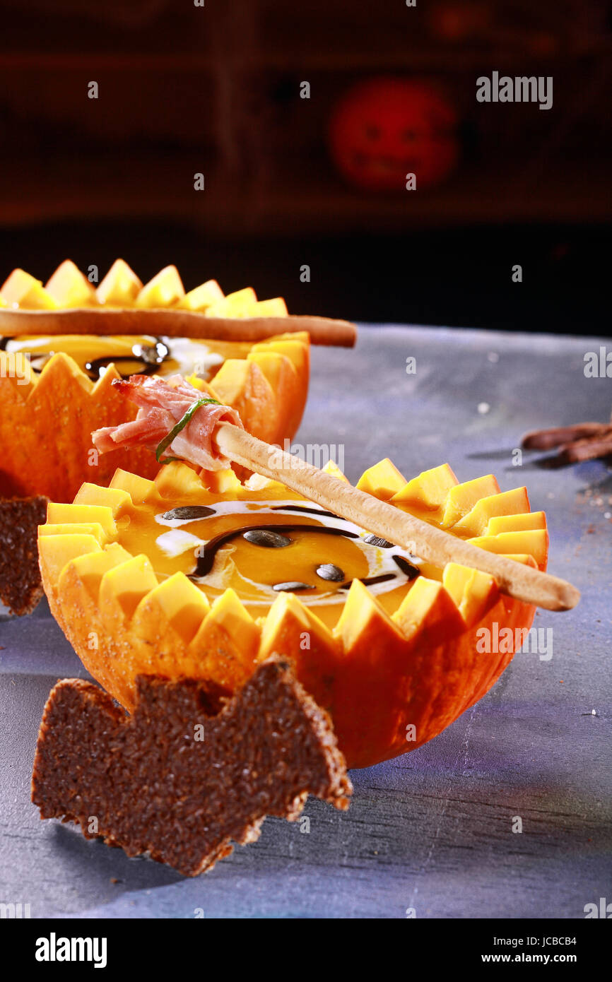 Halloween Pumpkin Soup with Bat Shaped Toast Crouton Served in Half Pumpkins Stock Photo