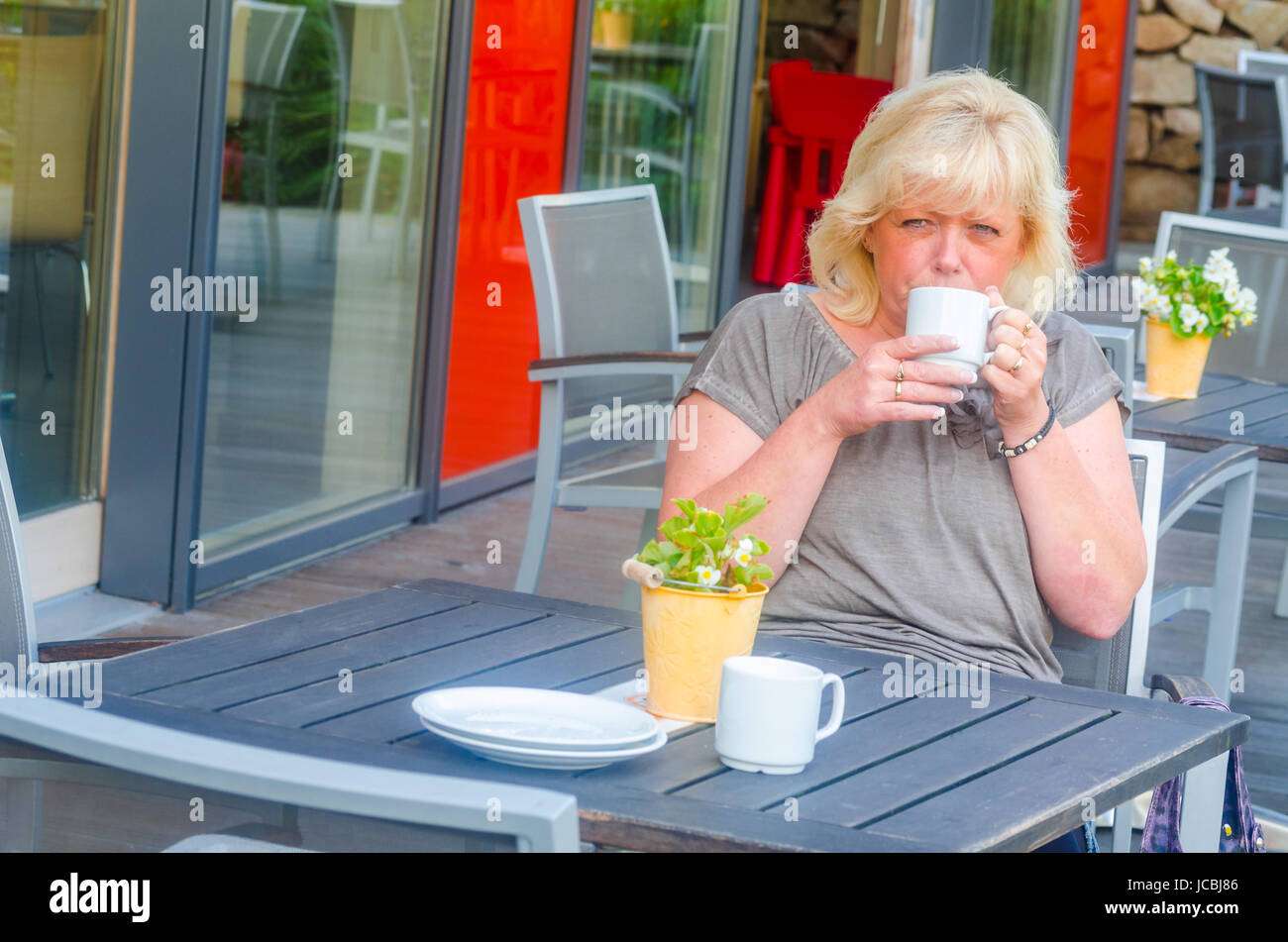 Frau sitzt in einem Straßencafe entspannt an einem Tisch, genießt den Tag. Stock Photo