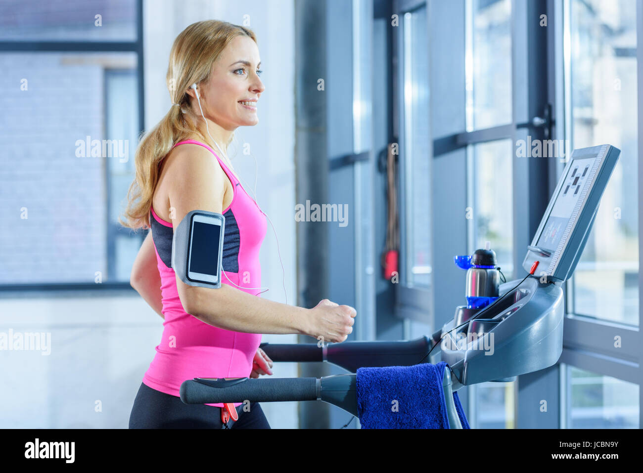 Side view of sporty blonde woman exercising on treadmill in gym Stock