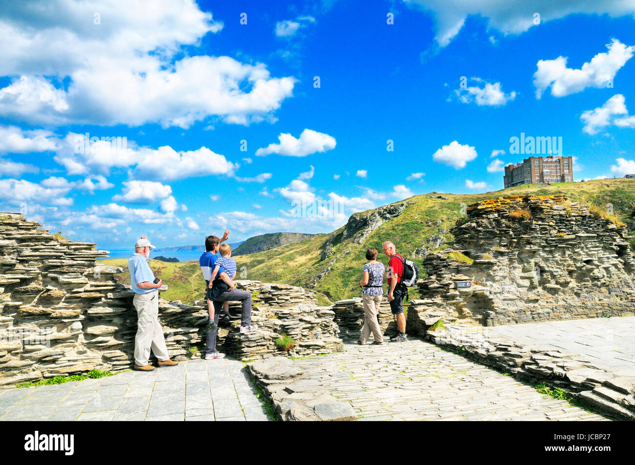 Tourists at the historic site of Tintagel Castle with Camelot Castle Hotel perched high on a cliff top, Cornwall, England, UK Stock Photo