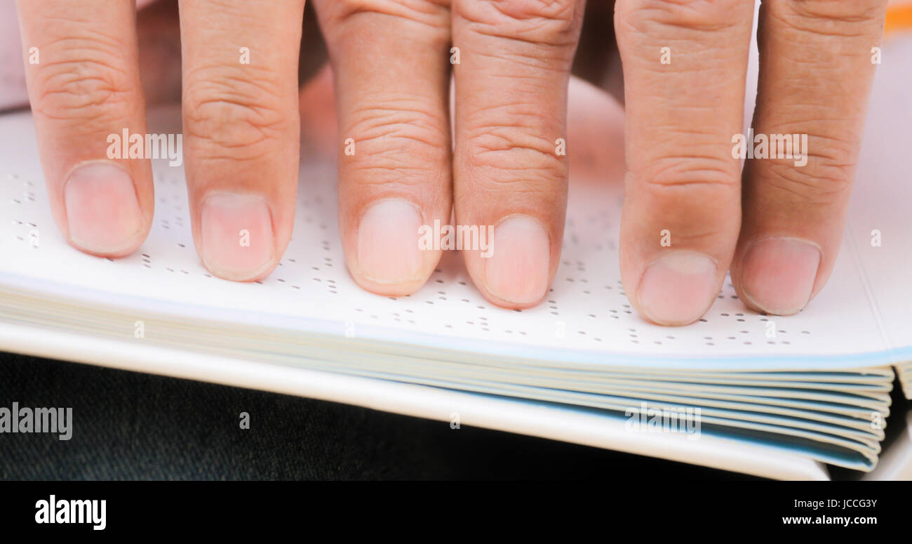 Hispanic blind man, people with disability, handicapped person and everyday life. Visually impaired man reading book with hands, touching page written Stock Photo