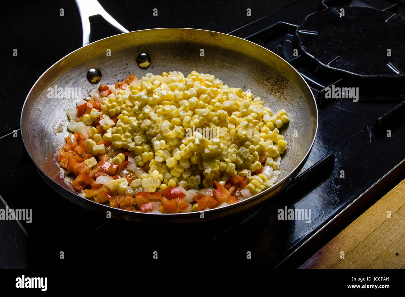 Sweet corn red peppers and onions in fry pan on the stove Stock Photo