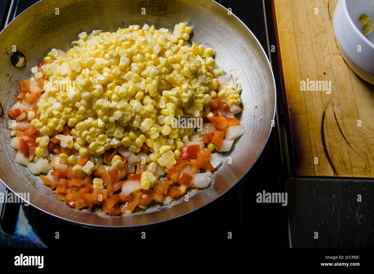 Sweet corn red peppers and onions in fry pan on the stove Stock Photo