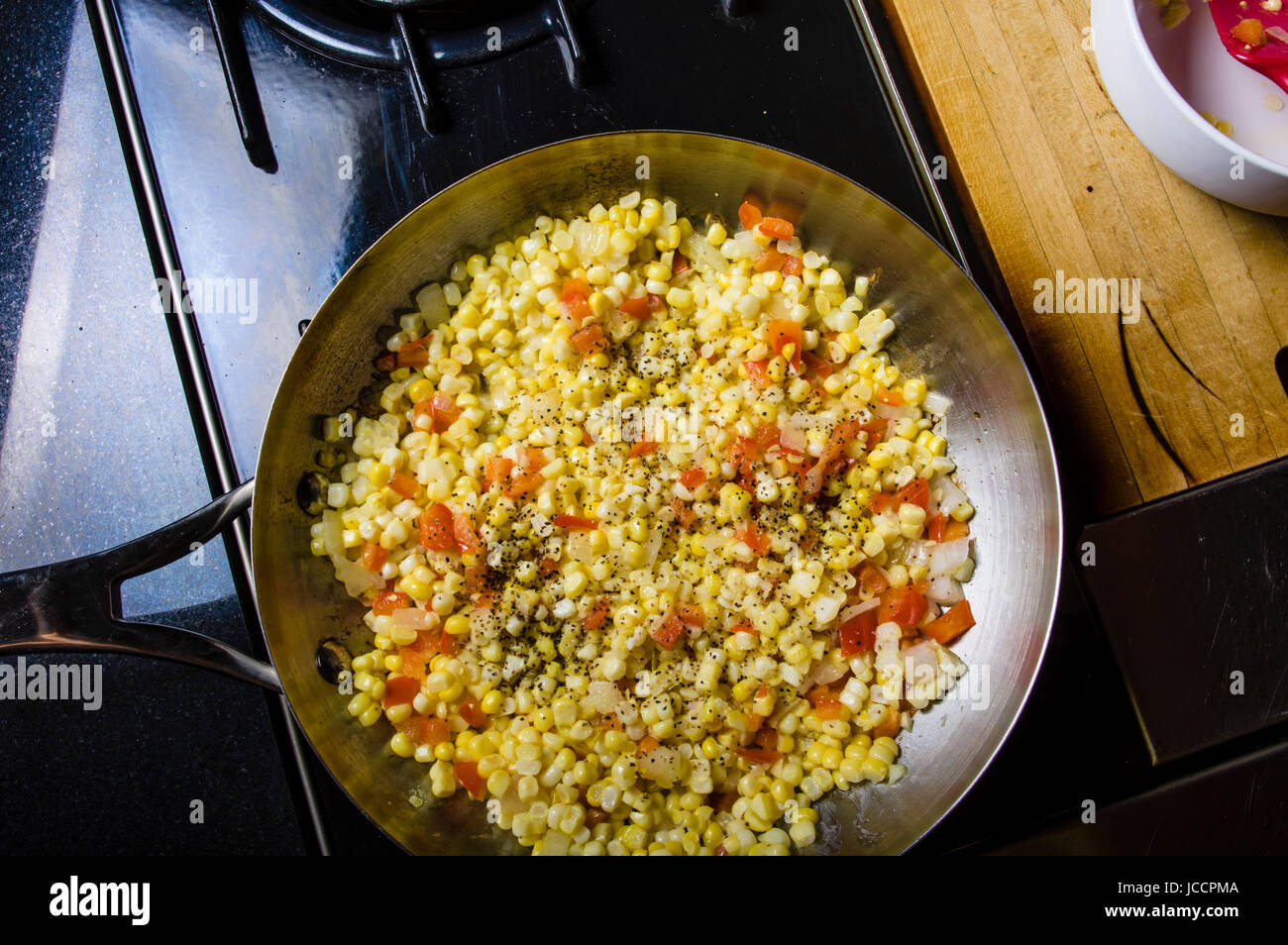 Sweet corn red peppers and onions in fry pan on the stove Stock Photo