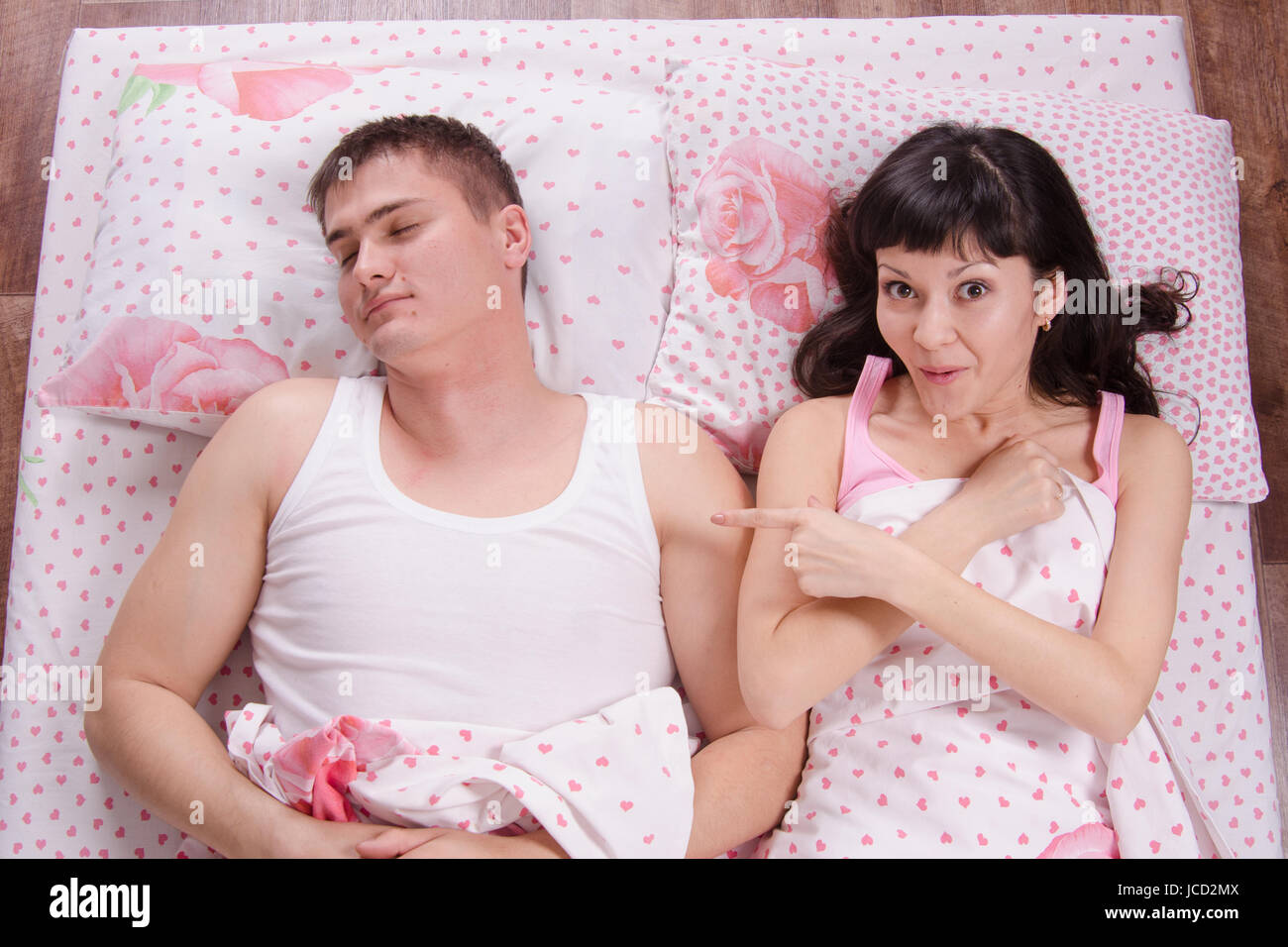 A young girl waking up in the morning sees a stranger guy in bed Stock