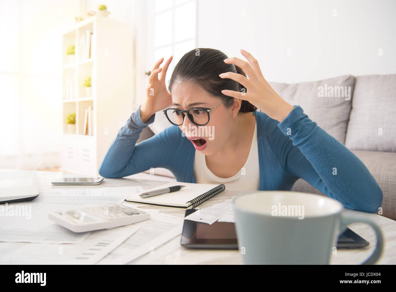 shocked crazy woman checking expensive electricity and household bills sitting on sofa in the living room at home. finance interior and domestic house Stock Photo