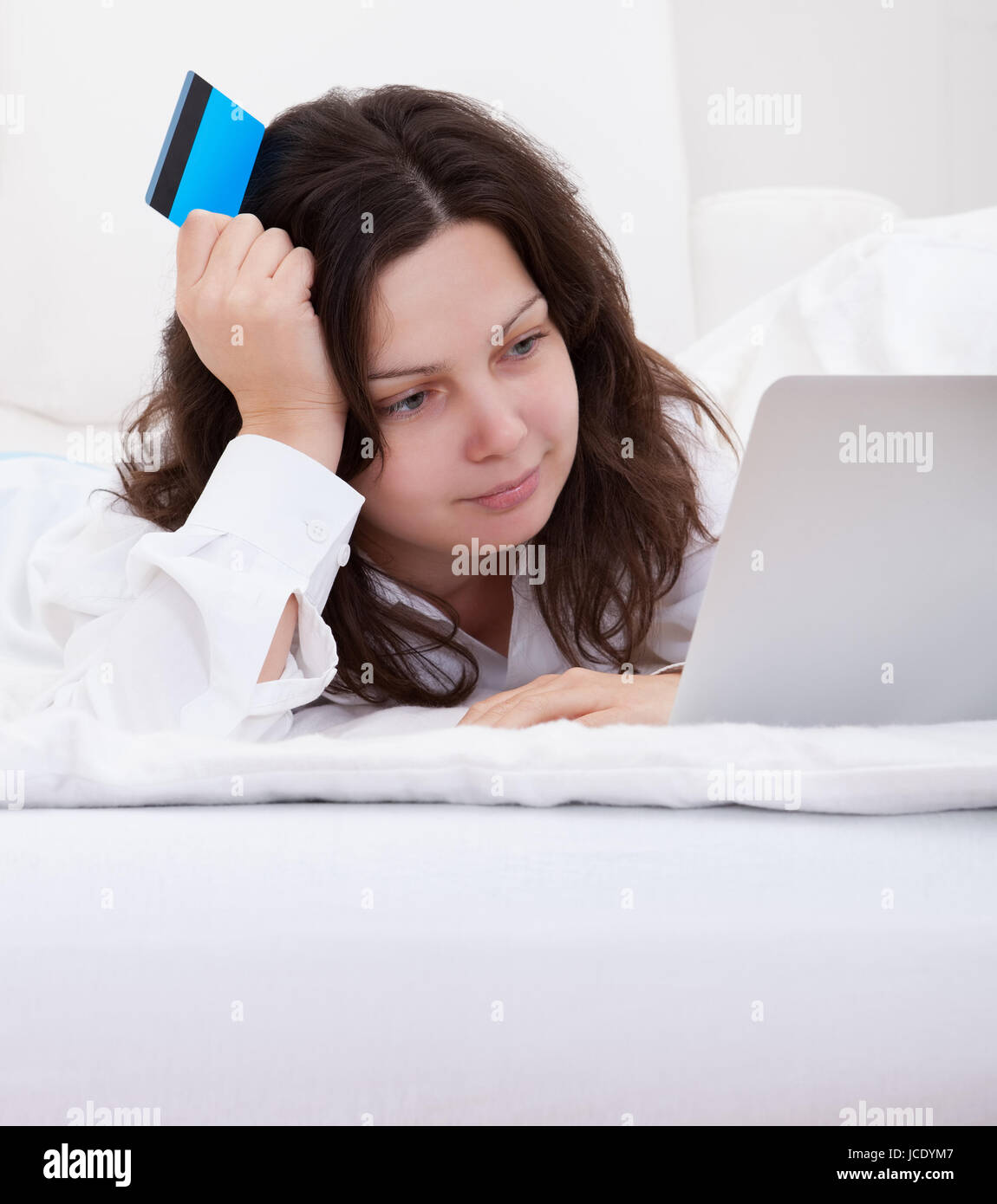 Excited Attractive Young Woman Lying On Her Bed With Her Laptop Making Purchases Online With Her