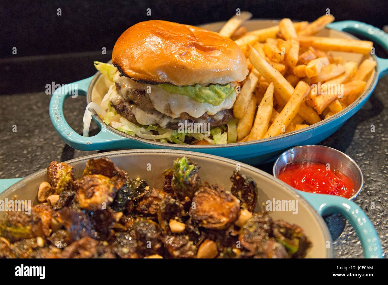 A cheese burger served with fries in Calgary, Canada. The dish is served with seared brussel sprouts with almonds and lime juice. Stock Photo