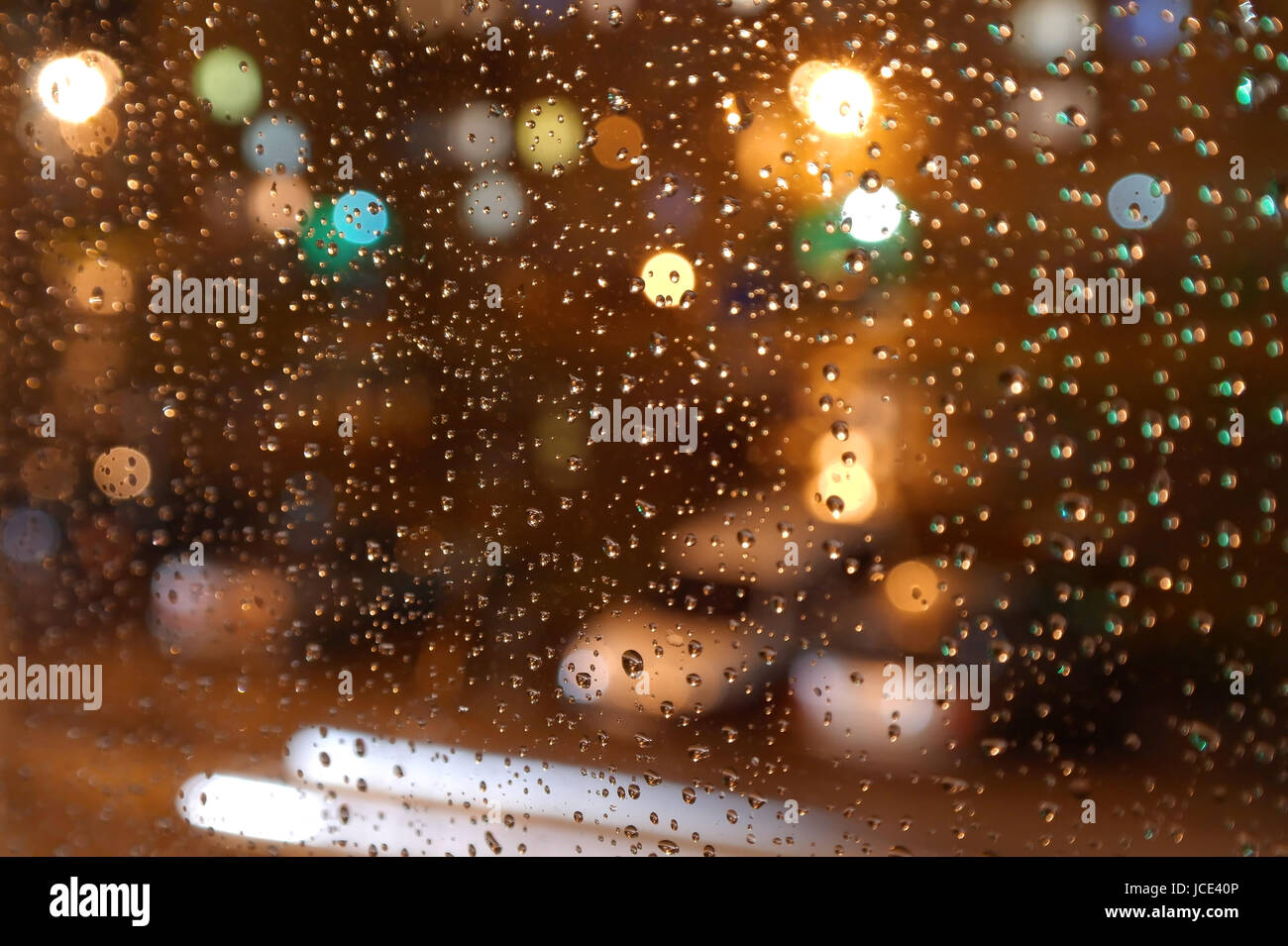 Droplets of night rain on window, on back plan washed away lights of the torches. Shallow DOF Stock Photo