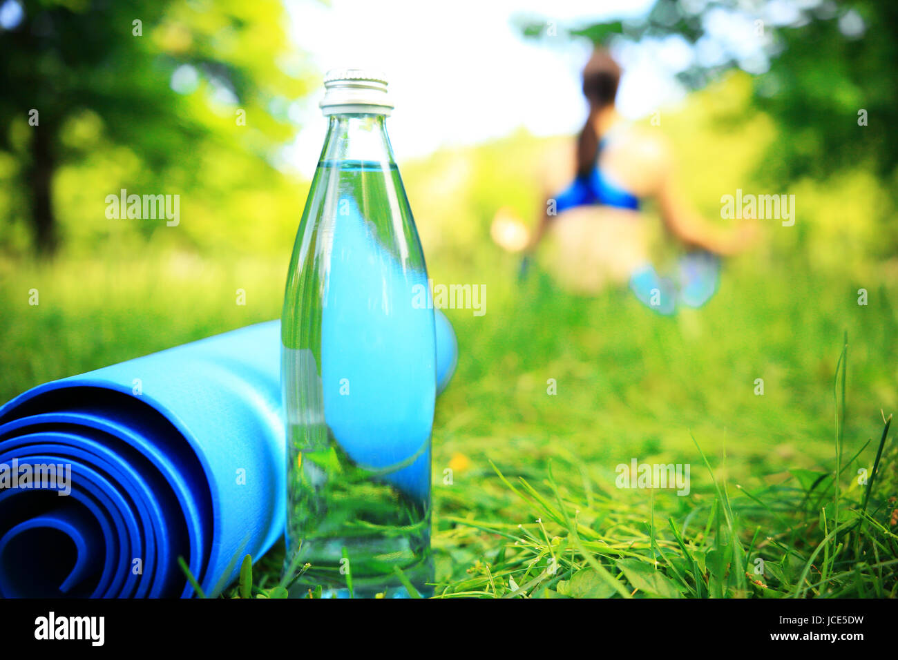 Healthy lifestyle background. Bottle of water and gym mat on relaxing girl background on a sunny summer day outdoors. Stock Photo